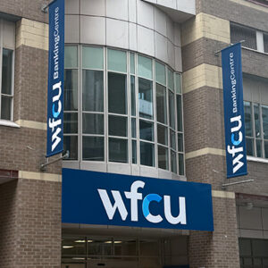 Exterior view of the WFCU Banking Centre Grenville Toronto branch featuring a blue WFCU entrance sign and two vertical BankingCentre banners mounted on a multi-storey brick and glass building.