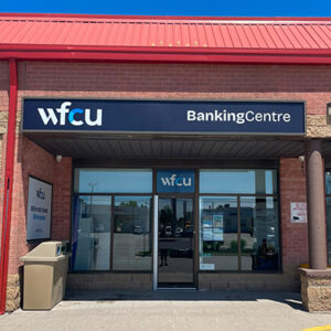 Exterior view of the WFCU Banking Centre Midland branch showing the main entrance beneath a blue 'WFCU BankingCentre' sign. The branch features glass doors and windows within a red brick building.
