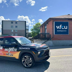 Exterior view of the WFCU Banking Centre North Bay branch. A WFCU-branded building with a large 'WFCU BankingCentre' sign is shown beside a parked promotional vehicle displaying WFCU and local radio station branding.