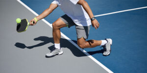 Person on an outdoor pickleball court lunging with a paddle to return a ball.