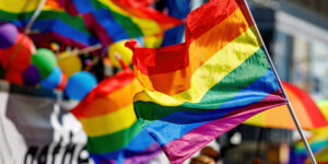 Rainbow Pride flags displayed at a community event, with colourful decorations and attendees visible in the background.