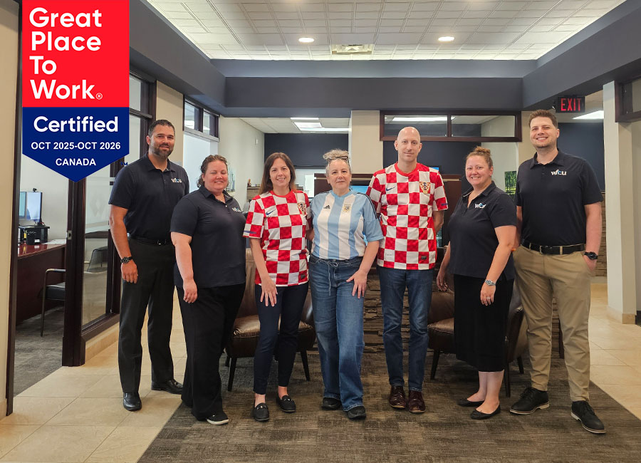 Group photo of six WFCU team members standing inside a branch or office lobby. Three team members are wearing soccer jerseys, while three are wearing WFCU-branded shirts. A 'Great Place to Work Certified Canada, October 2025–October 2026' badge appears in the upper-left corner of the image.